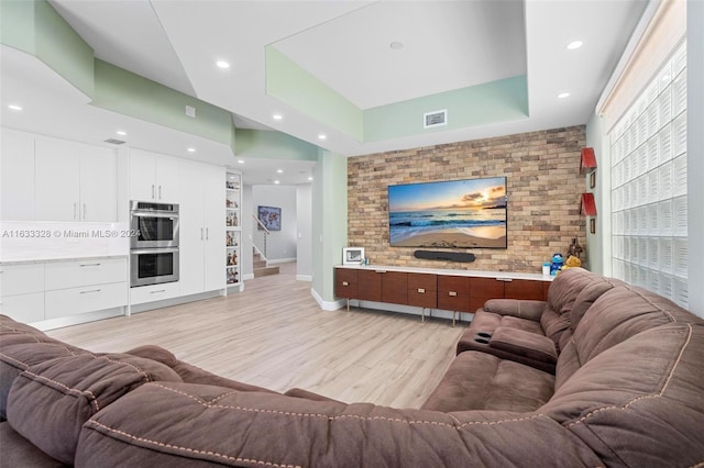 living room with light hardwood / wood-style floors, a raised ceiling, and brick wall