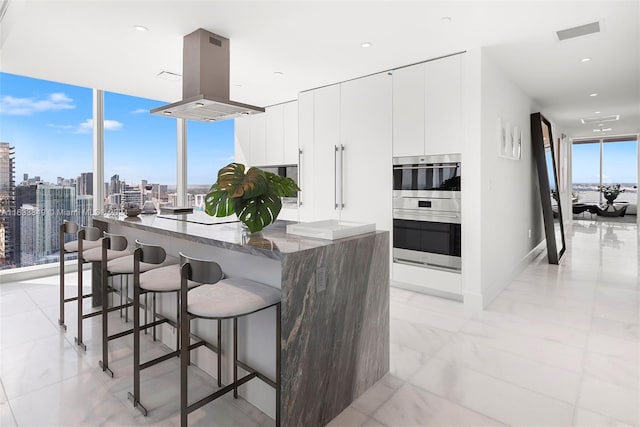 kitchen with visible vents, island exhaust hood, a wall of windows, modern cabinets, and double oven