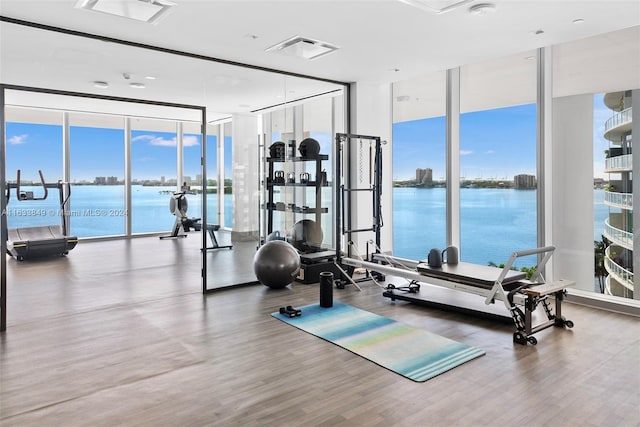 exercise room with a water view, a wall of windows, visible vents, and wood finished floors