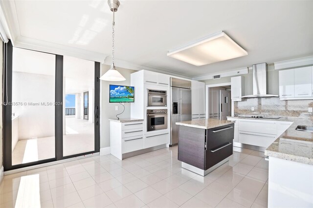 kitchen with wall chimney range hood, stainless steel appliances, hanging light fixtures, decorative backsplash, and a center island