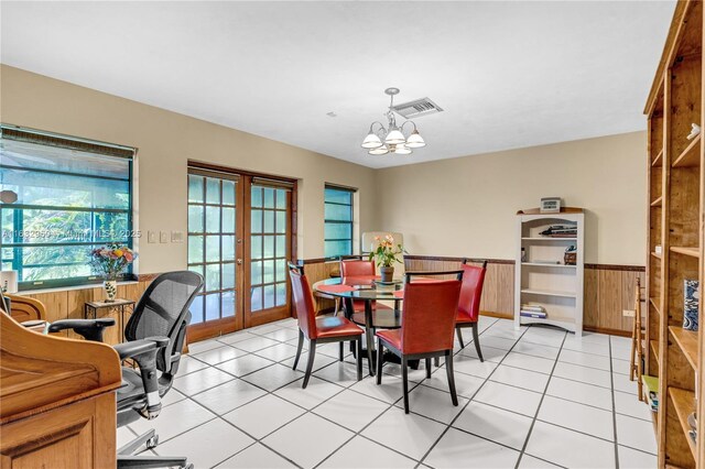 dining room featuring french doors, wooden walls, light tile patterned flooring, and a notable chandelier