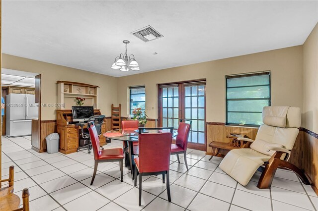 tiled dining area with wood walls, a chandelier, and french doors