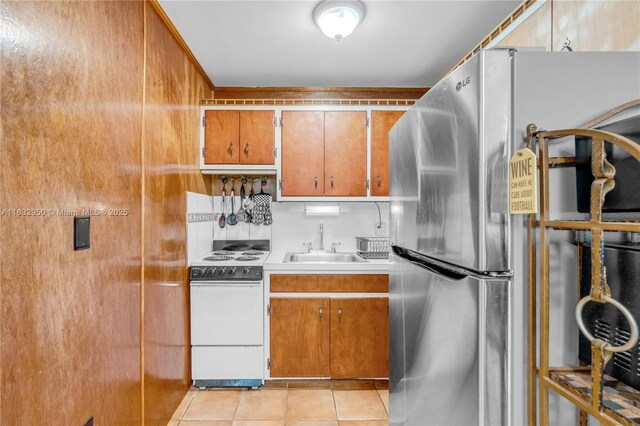 kitchen with sink, light tile patterned floors, stainless steel fridge, and white range with electric stovetop