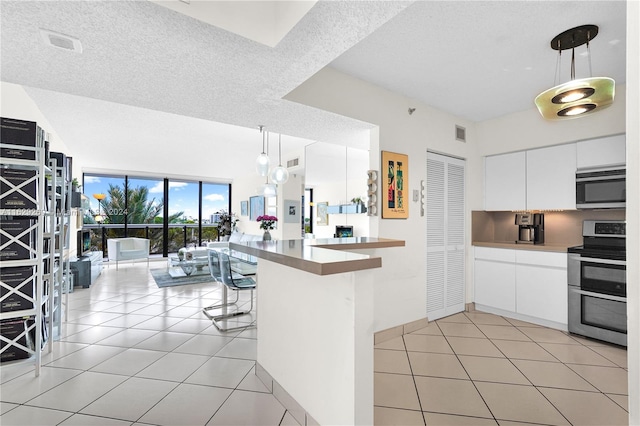 kitchen with appliances with stainless steel finishes, white cabinets, pendant lighting, light tile patterned floors, and a kitchen breakfast bar