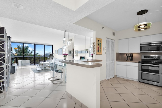 kitchen with hanging light fixtures, stainless steel appliances, light tile patterned floors, and white cabinets