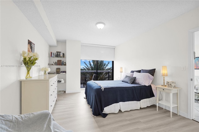 bedroom featuring access to exterior, light wood-type flooring, and a textured ceiling