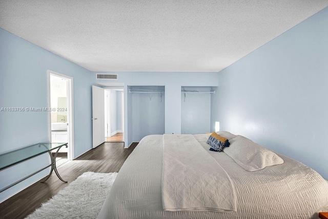 bedroom with dark wood-type flooring, a textured ceiling, and ensuite bathroom