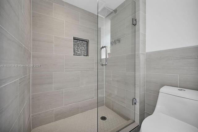 bathroom featuring a shower with door, tile walls, and toilet