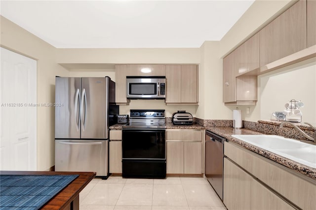 kitchen with appliances with stainless steel finishes, dark stone counters, light tile patterned floors, and light brown cabinets