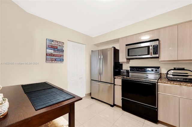 kitchen featuring light tile patterned flooring, stainless steel appliances, dark stone countertops, and light brown cabinetry