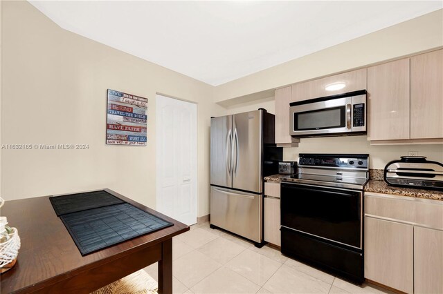 5757 Collins Ave Unit 801, Miami Beach, FL 33140 - kitchen with appliances with stainless steel finishes, light brown cabinetry, dark stone countertops, and light tile patterned floors