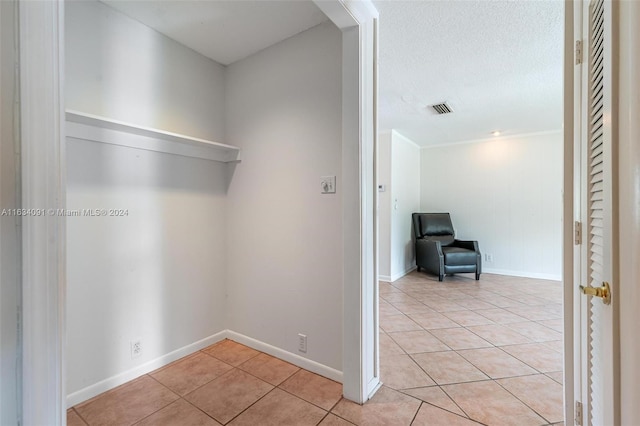 interior space featuring a textured ceiling, light tile patterned floors, and crown molding