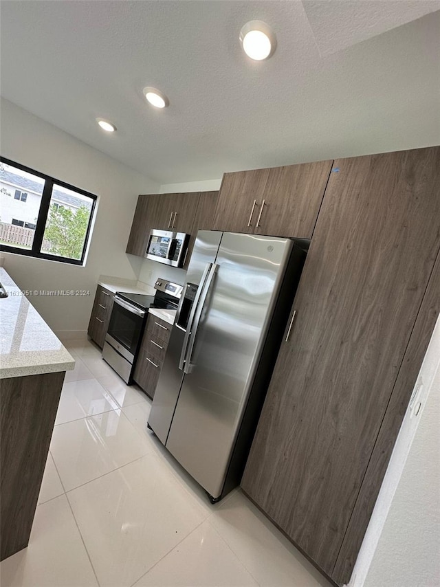 kitchen with appliances with stainless steel finishes, light tile patterned floors, and a textured ceiling