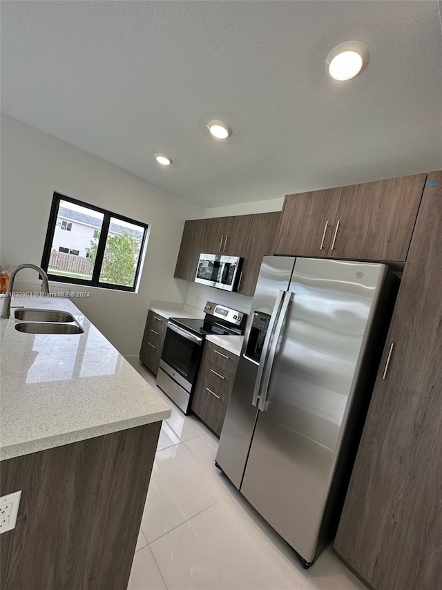 kitchen featuring sink, appliances with stainless steel finishes, light stone counters, and light tile patterned floors