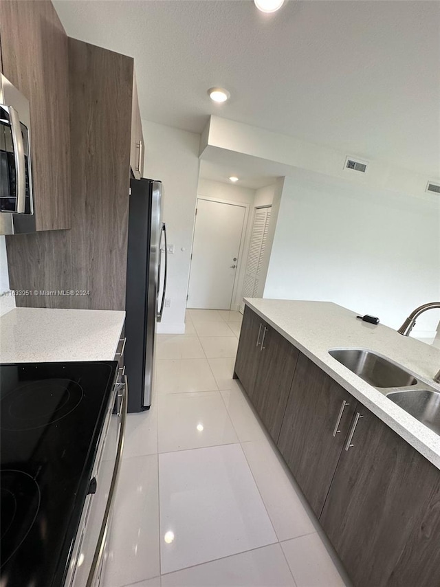 kitchen featuring stainless steel appliances, sink, dark brown cabinets, and light tile patterned floors