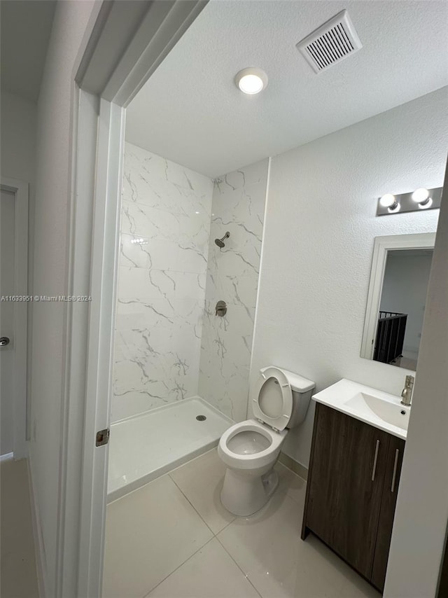 bathroom featuring vanity, tiled shower, tile patterned floors, toilet, and a textured ceiling