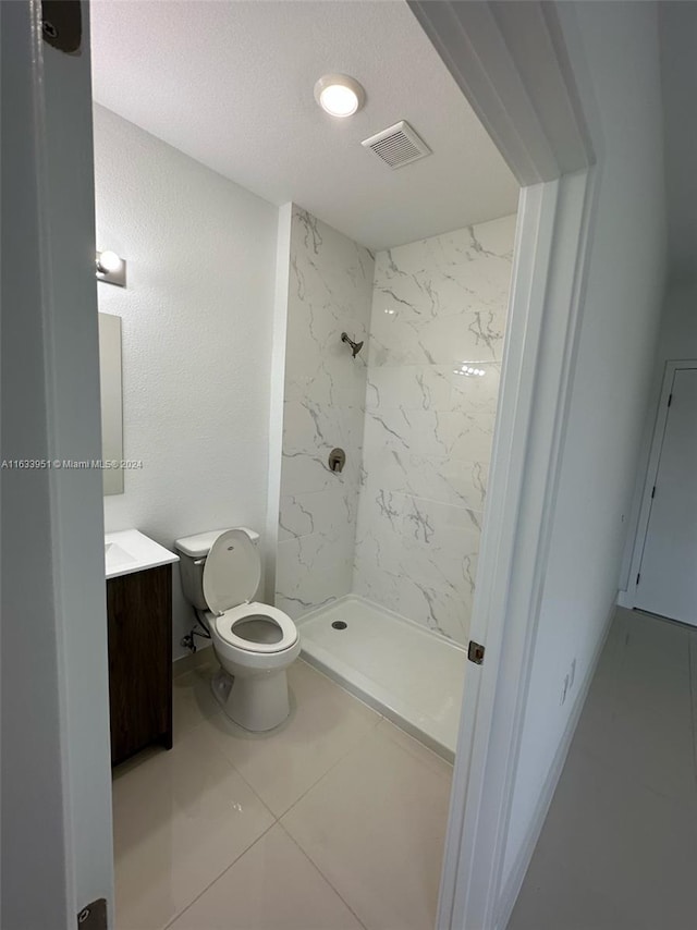 bathroom featuring tile patterned flooring, a tile shower, a textured ceiling, toilet, and vanity