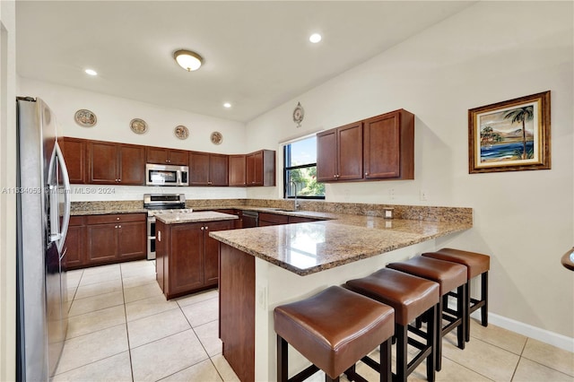 kitchen with a kitchen bar, stove, kitchen peninsula, fridge, and light tile patterned floors