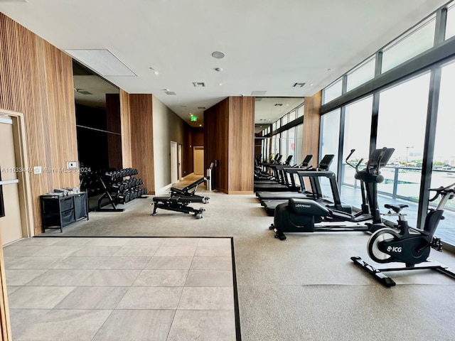 workout area featuring light tile patterned flooring, wooden walls, and floor to ceiling windows