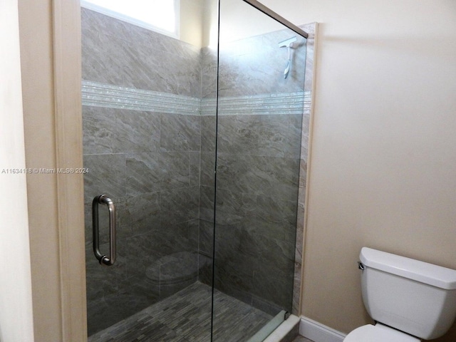 bathroom featuring a shower with door and toilet