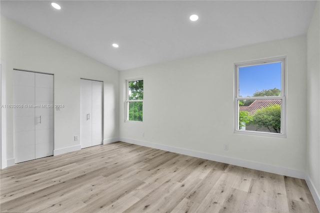 unfurnished bedroom featuring multiple closets, lofted ceiling, and light hardwood / wood-style flooring