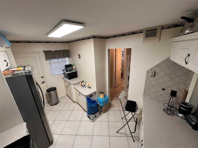 kitchen featuring light tile patterned flooring, stainless steel refrigerator, and white cabinets