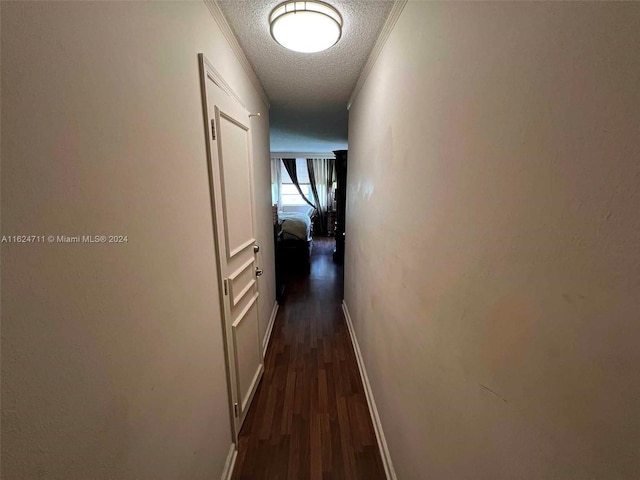 hall with dark wood-type flooring, ornamental molding, and a textured ceiling