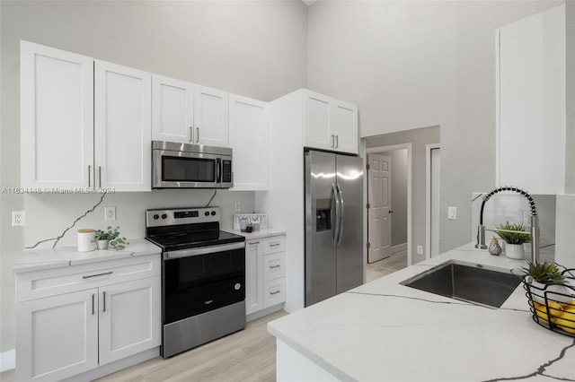 kitchen with white cabinetry, sink, light stone counters, light hardwood / wood-style floors, and appliances with stainless steel finishes