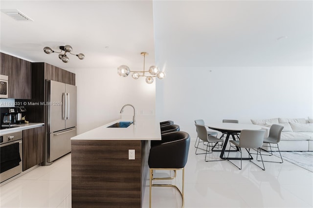 kitchen featuring appliances with stainless steel finishes, sink, hanging light fixtures, light tile patterned floors, and a kitchen island with sink