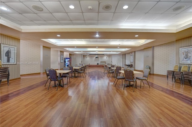 dining room with a raised ceiling, wood-type flooring, brick wall, and a drop ceiling