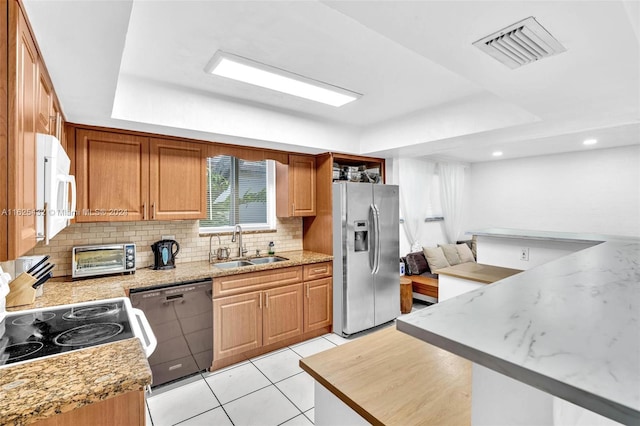 kitchen with sink, light tile patterned floors, appliances with stainless steel finishes, backsplash, and light stone counters