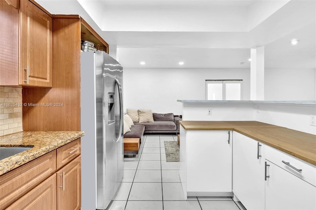 kitchen with light stone counters, backsplash, stainless steel fridge, and light tile patterned flooring