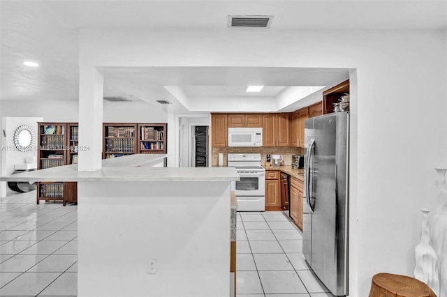 kitchen with tasteful backsplash, light tile patterned floors, kitchen peninsula, a raised ceiling, and white appliances