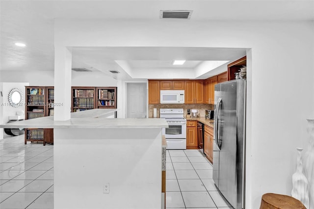 kitchen with light tile patterned flooring, tasteful backsplash, a tray ceiling, kitchen peninsula, and white appliances