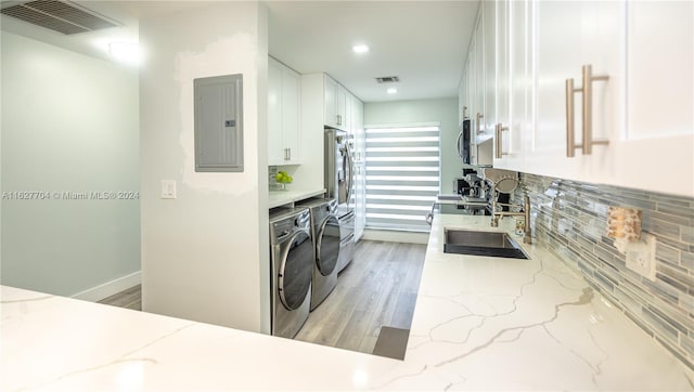 laundry area featuring electric panel, washer and clothes dryer, light hardwood / wood-style flooring, and sink