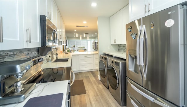 kitchen with light stone counters, light hardwood / wood-style floors, appliances with stainless steel finishes, backsplash, and washing machine and clothes dryer