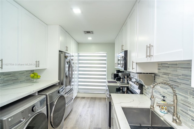 kitchen featuring separate washer and dryer, backsplash, light stone counters, stainless steel appliances, and light hardwood / wood-style floors