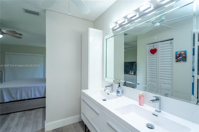 bathroom with a textured ceiling, double sink vanity, hardwood / wood-style floors, and ceiling fan