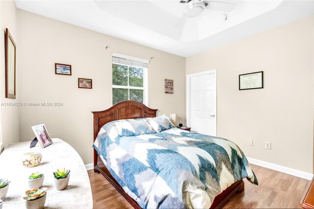 bedroom with a raised ceiling, ceiling fan, and light hardwood / wood-style flooring