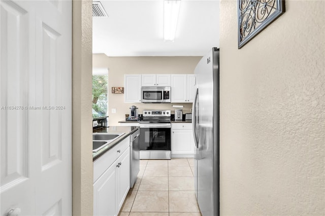 kitchen with light tile patterned flooring, appliances with stainless steel finishes, white cabinetry, and sink