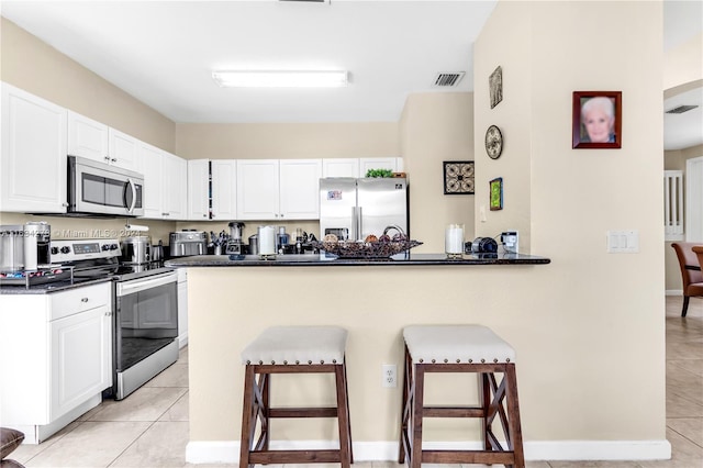 kitchen featuring stainless steel appliances, white cabinets, kitchen peninsula, a breakfast bar area, and light tile patterned flooring