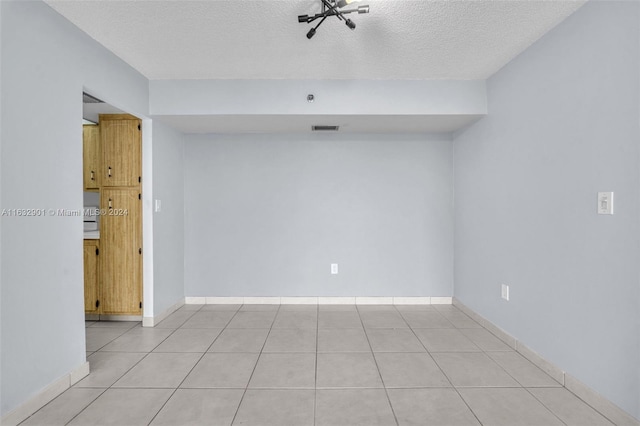 tiled spare room featuring a textured ceiling and an inviting chandelier