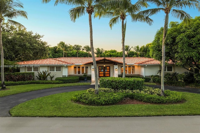 single story home featuring stucco siding, a tile roof, a front lawn, and curved driveway