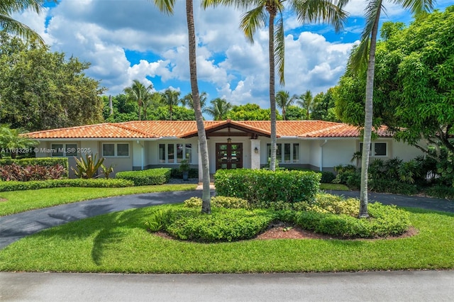 ranch-style house with french doors, a tile roof, a front yard, and stucco siding