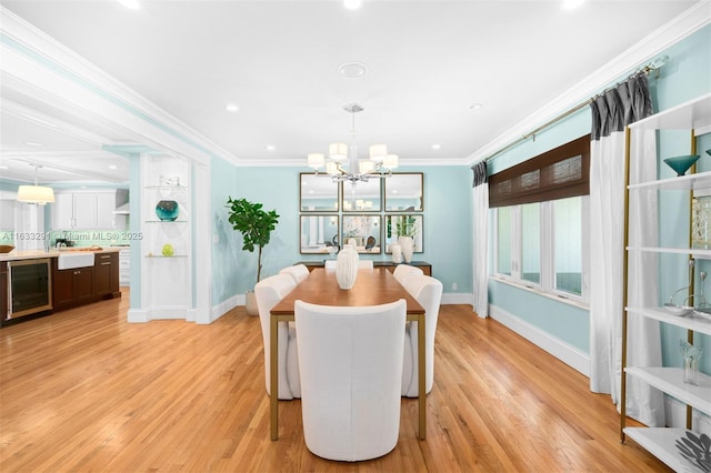 dining room with a notable chandelier, light wood-type flooring, crown molding, and beverage cooler