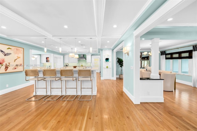 kitchen with coffered ceiling, wall chimney range hood, beamed ceiling, hanging light fixtures, and a breakfast bar area