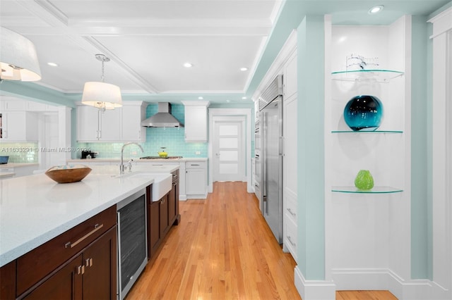 kitchen with wall chimney range hood, dark brown cabinets, decorative light fixtures, white cabinetry, and wine cooler