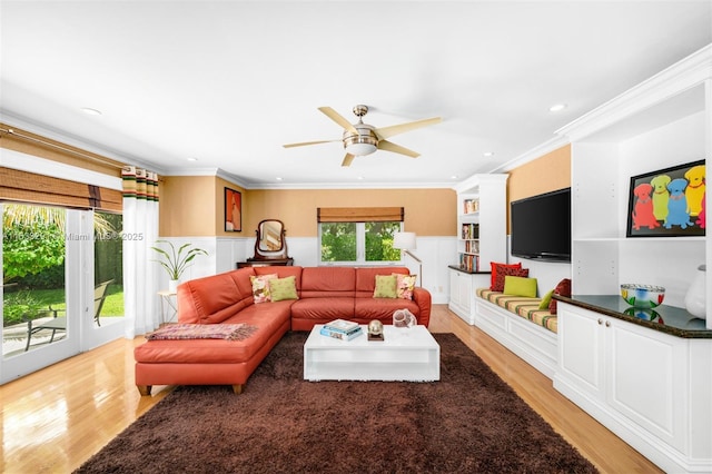living area with light wood finished floors, ceiling fan, a wainscoted wall, and ornamental molding
