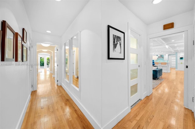 corridor with arched walkways, baseboards, recessed lighting, and light wood-style floors