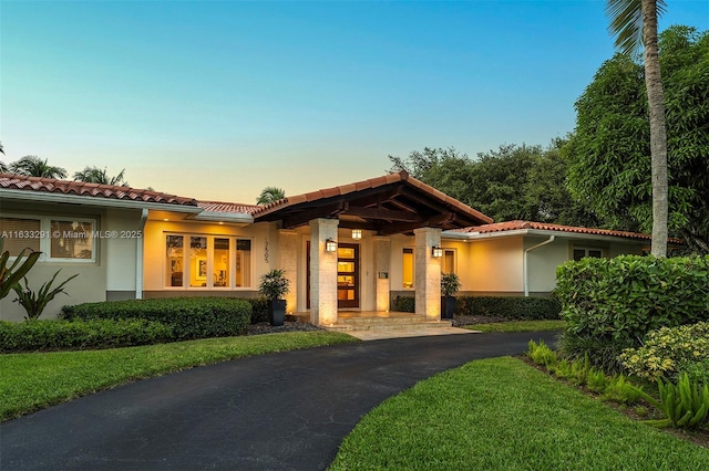 view of front facade with a tiled roof, driveway, a yard, and stucco siding